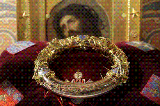 crown of thorns in ornate gold and crystal reliquary on velvet cushion in front of portrait of jesus wearing crown